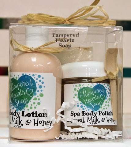 Front of gift pack, clear plastic box with cream bow, travel sized items include cream lotion, brown body polish and full-sized tan soap bar.